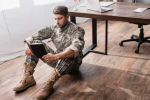 Focused,Military,Man,In,Uniform,Holding,Copy,Book,While,Sitting